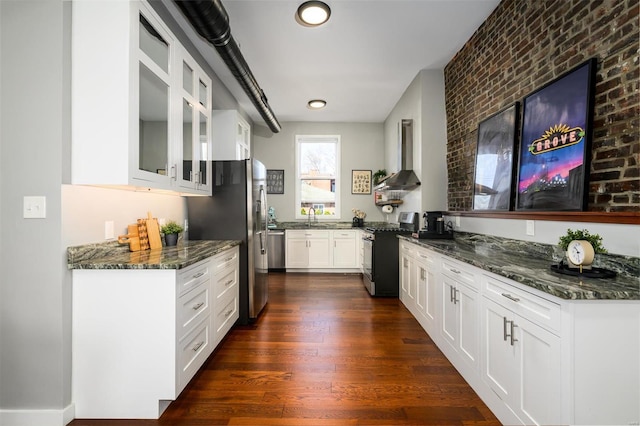 kitchen featuring dark wood-style floors, a sink, stainless steel appliances, glass insert cabinets, and wall chimney range hood