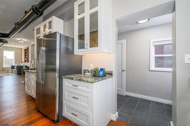 kitchen with stainless steel refrigerator with ice dispenser, stone countertops, open floor plan, white cabinetry, and glass insert cabinets