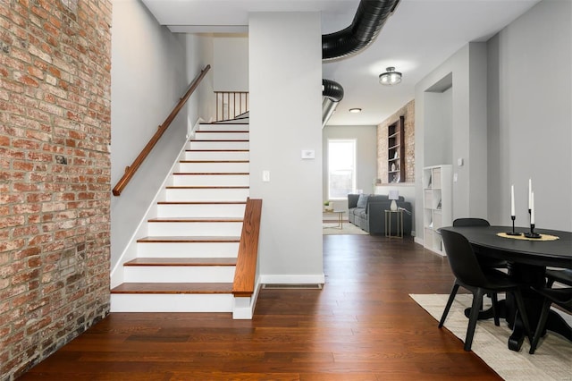 stairs featuring built in features, wood finished floors, baseboards, and brick wall