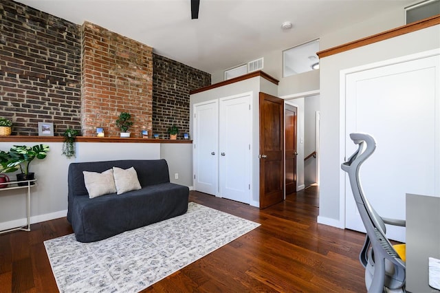 sitting room with visible vents, baseboards, wood finished floors, and brick wall