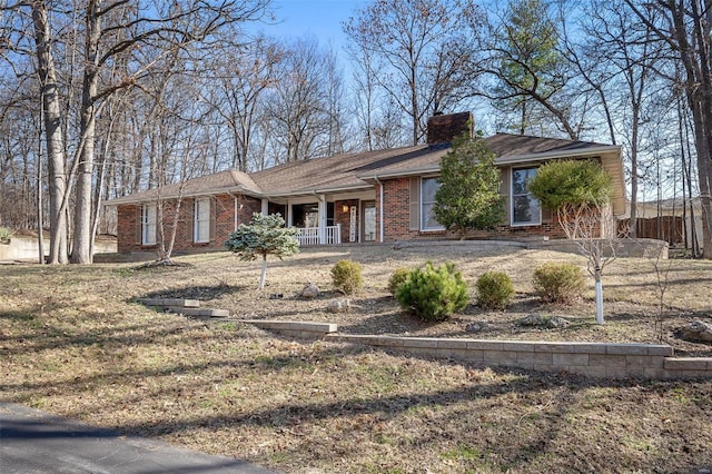 ranch-style house with a porch, fence, brick siding, and a chimney