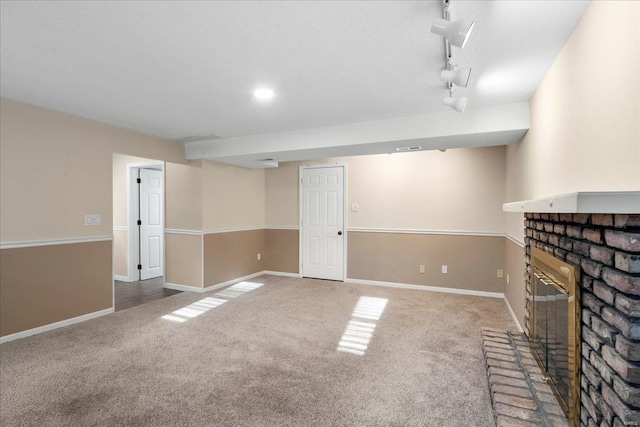 unfurnished living room featuring a brick fireplace, baseboards, rail lighting, and carpet