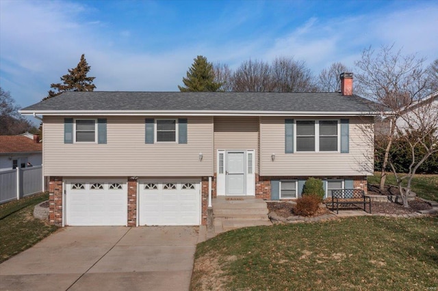 split foyer home with concrete driveway, a front yard, roof with shingles, a chimney, and an attached garage