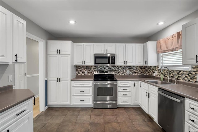 kitchen with dark countertops, tasteful backsplash, stainless steel appliances, white cabinetry, and a sink