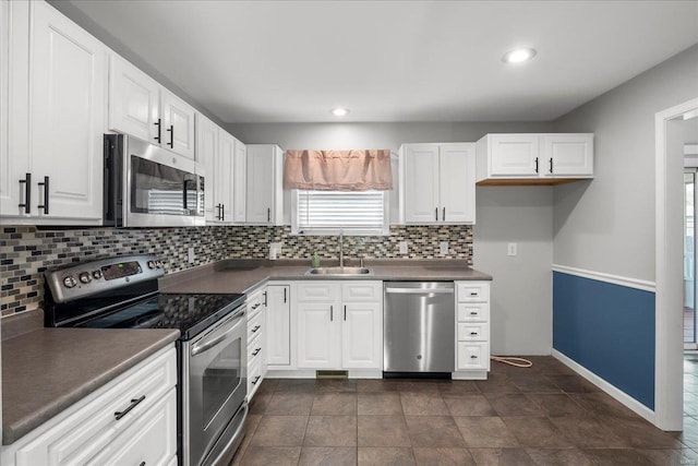 kitchen with dark countertops, decorative backsplash, stainless steel appliances, white cabinetry, and a sink