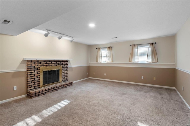 unfurnished living room featuring visible vents, carpet floors, rail lighting, baseboards, and a brick fireplace