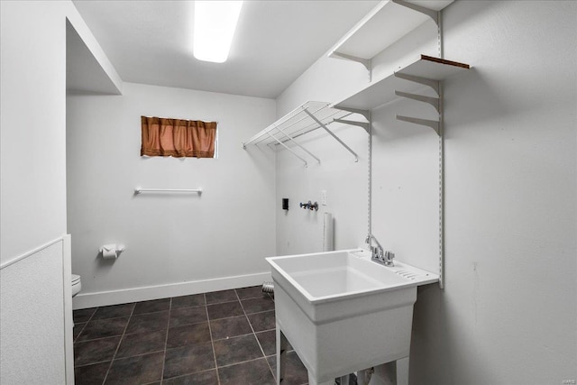 washroom featuring a sink, baseboards, dark tile patterned floors, and laundry area