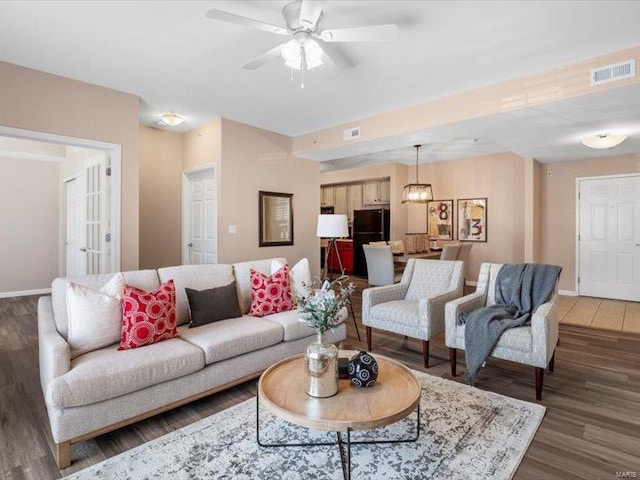 living area with a ceiling fan, wood finished floors, visible vents, and baseboards