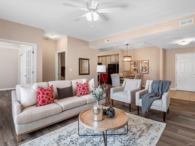 living room featuring visible vents, baseboards, wood finished floors, and a ceiling fan