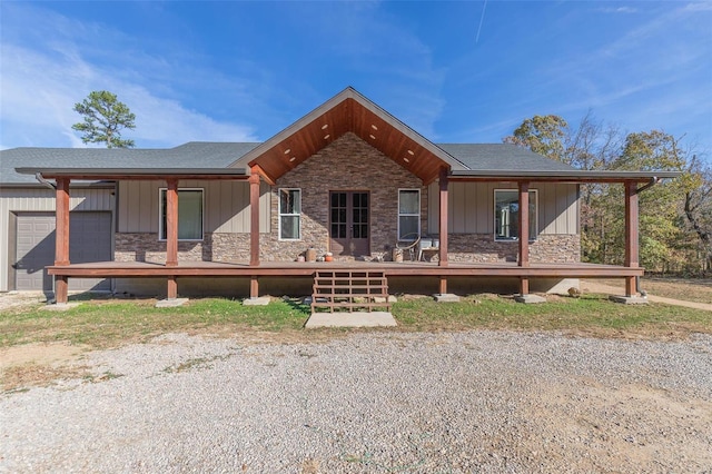 view of front facade featuring stone siding, covered porch, an attached garage, and roof with shingles