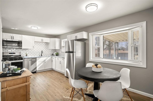 kitchen featuring tasteful backsplash, light wood-type flooring, light countertops, white cabinets, and stainless steel appliances