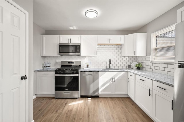 kitchen featuring a sink, light stone counters, light wood-style floors, appliances with stainless steel finishes, and white cabinets