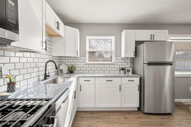 kitchen featuring light stone counters, light wood finished floors, a sink, appliances with stainless steel finishes, and white cabinetry