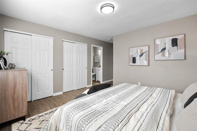 bedroom with ensuite bath, wood finished floors, multiple closets, and baseboards