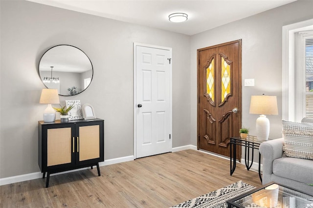 foyer featuring light wood finished floors, an inviting chandelier, and baseboards