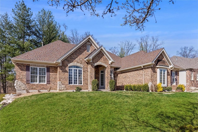 view of front facade with brick siding, a front lawn, and a shingled roof