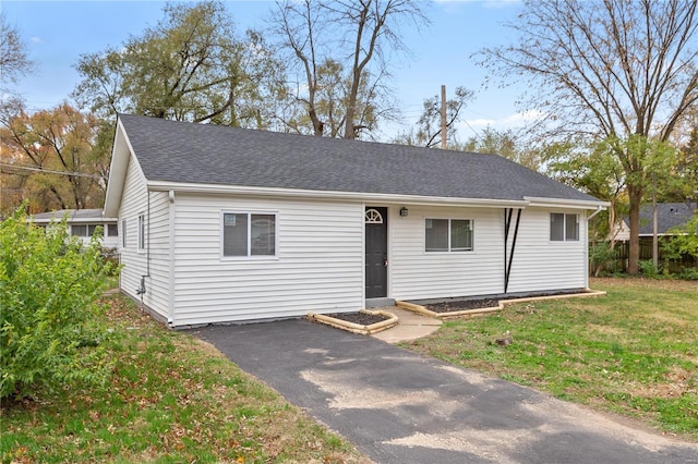 ranch-style home featuring aphalt driveway, a front lawn, roof with shingles, and fence