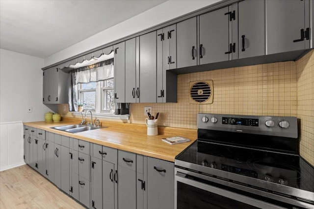 kitchen with light wood-style flooring, gray cabinets, electric stove, a sink, and tasteful backsplash