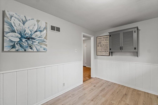 spare room featuring a wainscoted wall, wood finished floors, and visible vents