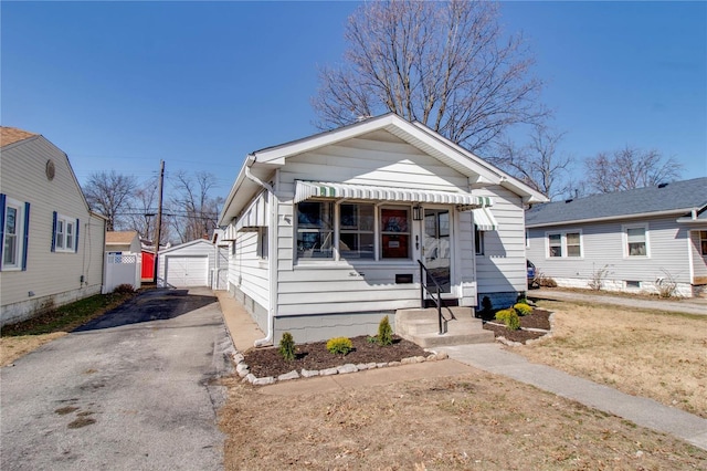 view of front of house featuring aphalt driveway, a detached garage, and an outbuilding