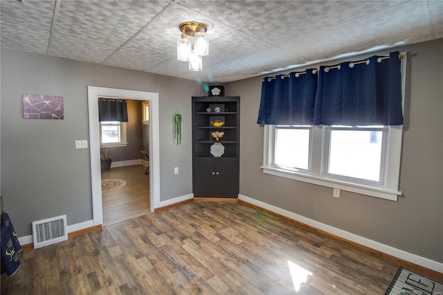 spare room with wood finished floors, visible vents, and baseboards