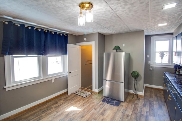 kitchen featuring light wood finished floors, blue cabinets, baseboards, and freestanding refrigerator