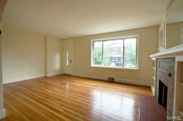 unfurnished living room with visible vents, a tile fireplace, baseboards, and wood finished floors