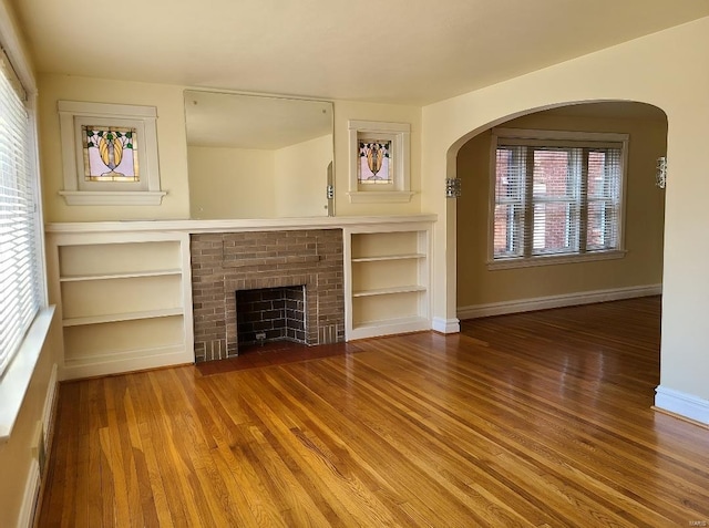 unfurnished living room featuring wood finished floors, built in shelves, a fireplace, and baseboards