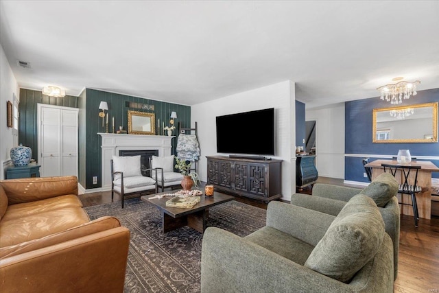 living room featuring visible vents, wood finished floors, a fireplace, baseboards, and a chandelier