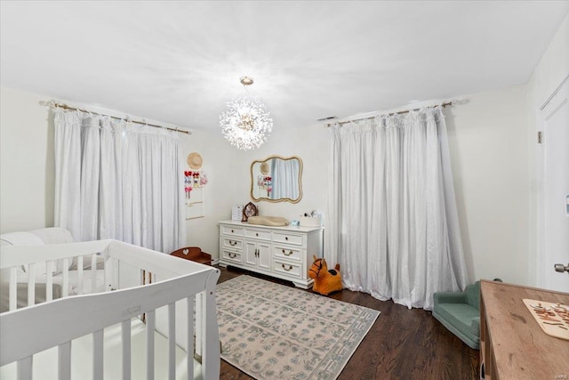 bedroom featuring a crib, a notable chandelier, and dark wood-style floors