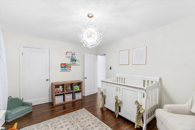 bedroom with a nursery area, a notable chandelier, and dark wood-style floors