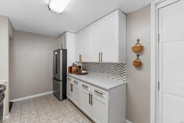 kitchen with backsplash, baseboards, light countertops, freestanding refrigerator, and white cabinets