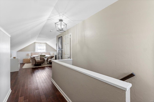 corridor with dark wood-type flooring, a notable chandelier, an upstairs landing, and vaulted ceiling