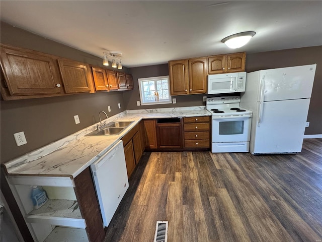 kitchen featuring visible vents, a sink, dark wood finished floors, white appliances, and brown cabinetry