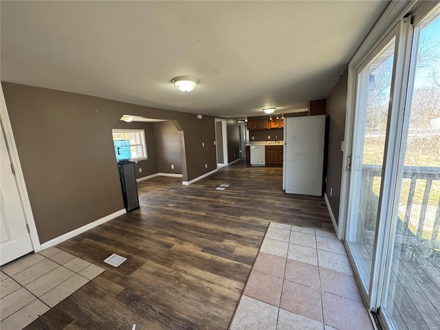 unfurnished living room with arched walkways, visible vents, dark wood finished floors, and baseboards