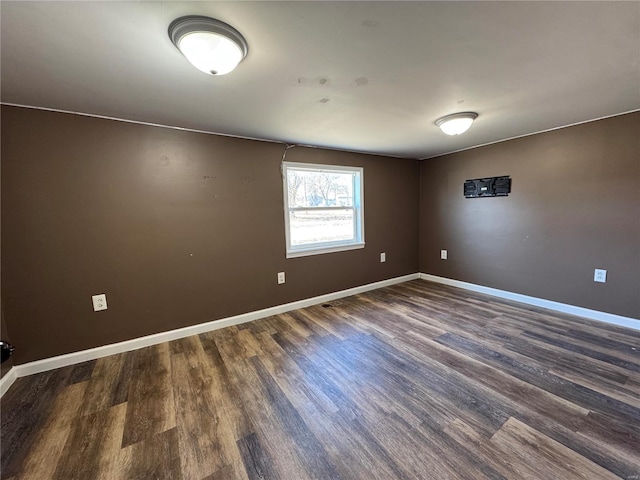 spare room featuring dark wood-type flooring and baseboards