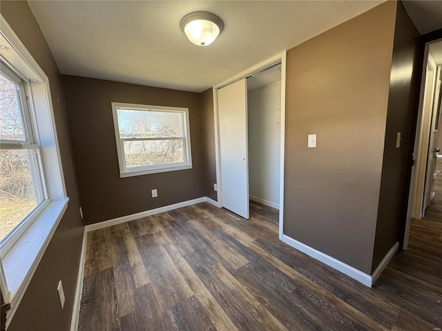 unfurnished bedroom with dark wood-style floors, a closet, and baseboards