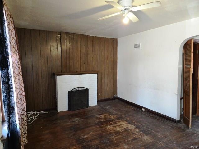 unfurnished living room with visible vents, a fireplace, dark wood-style flooring, arched walkways, and wood walls