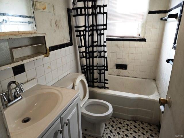 bathroom featuring toilet, tile walls, vanity, and  shower combination