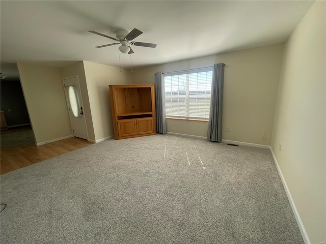 empty room featuring visible vents, light colored carpet, baseboards, and ceiling fan