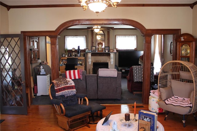 living area with ornamental molding, a ceiling fan, wood finished floors, arched walkways, and a fireplace