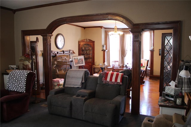 living area with wood finished floors, ornate columns, arched walkways, crown molding, and a notable chandelier