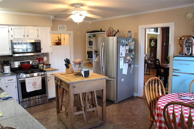 kitchen featuring dark tile patterned flooring, appliances with stainless steel finishes, white cabinets, and crown molding