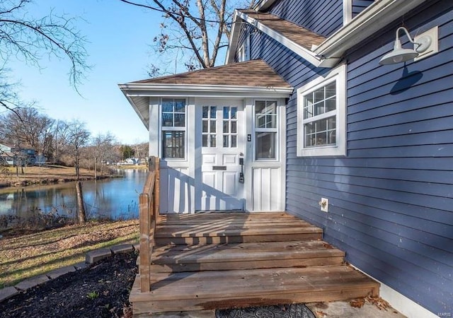 view of exterior entry with a water view and roof with shingles