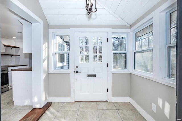 entryway featuring vaulted ceiling, light tile patterned floors, a healthy amount of sunlight, and baseboards