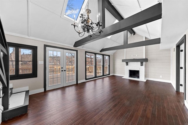 unfurnished living room with a healthy amount of sunlight, a large fireplace, beam ceiling, french doors, and wood-type flooring