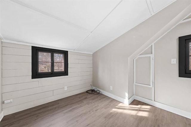 additional living space featuring wood walls, lofted ceiling, baseboards, and wood finished floors