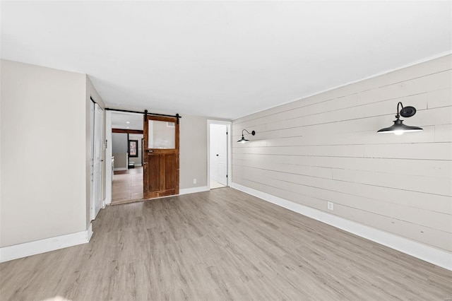 unfurnished room featuring baseboards, a barn door, and wood finished floors