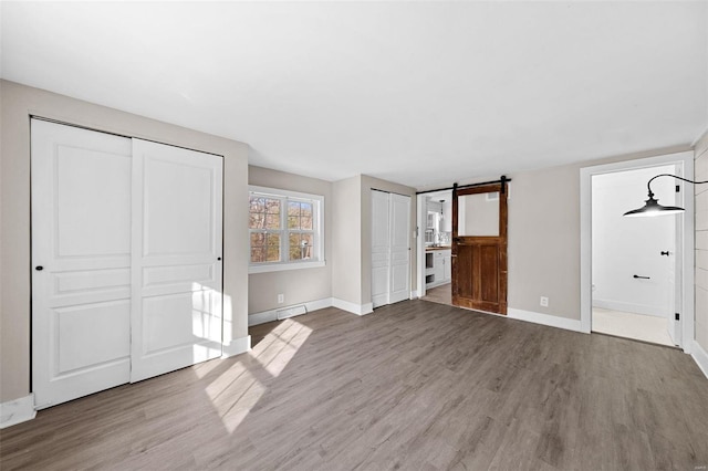 unfurnished bedroom featuring a barn door, baseboards, two closets, and wood finished floors