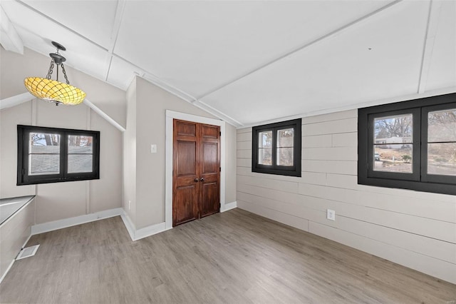 empty room featuring light wood-type flooring, visible vents, baseboards, and vaulted ceiling